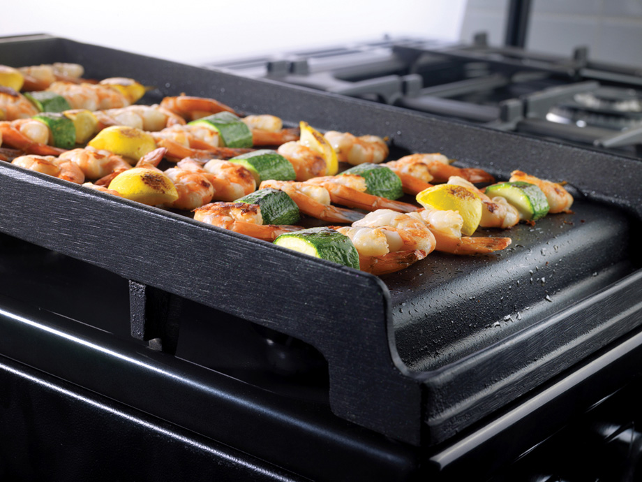 Frische Garnelen-Spieße mit Zucchini und Zitronenstücken werden auf einer gusseisernen Grillplatte auf einem Gasherd gegrillt