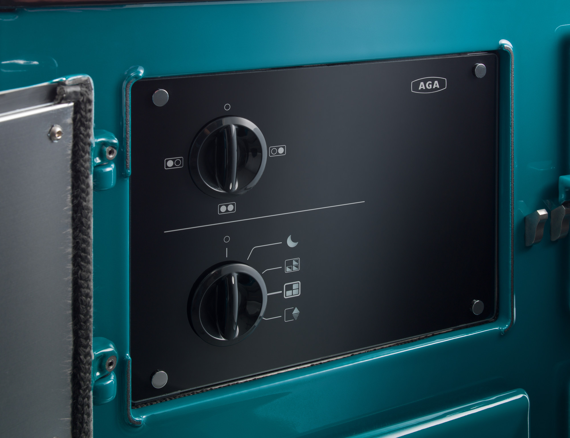 Detailaufnahme eines schwarzen Bedienfelds mit zwei Drehknöpfen und verschiedenen Symbolen an einem türkisfarbenen AGA Herd