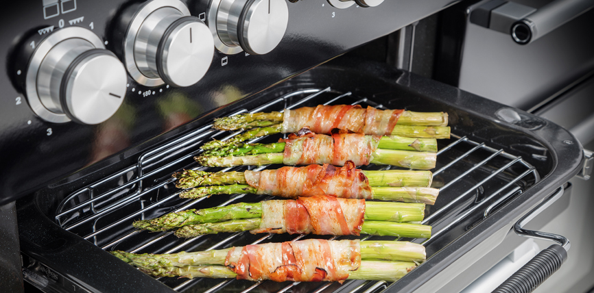 Grüner Spargel, mit knusprigem Speck umwickelt, wird auf einem Grillrost im Backofen zubereitet