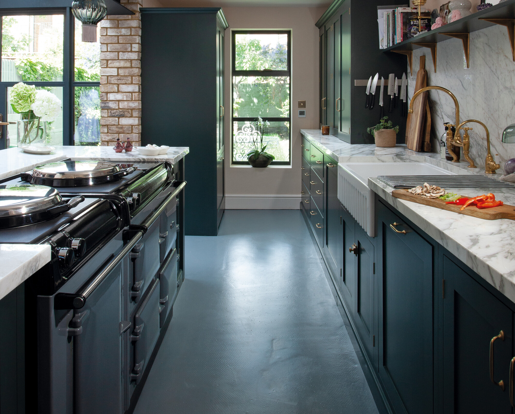 Elegante, moderne Küche mit dunkelgrünen Schränken, Marmorarbeitsplatten, goldenen Wasserhähnen und großen Fenstern, die viel Tageslicht hereinlassen.