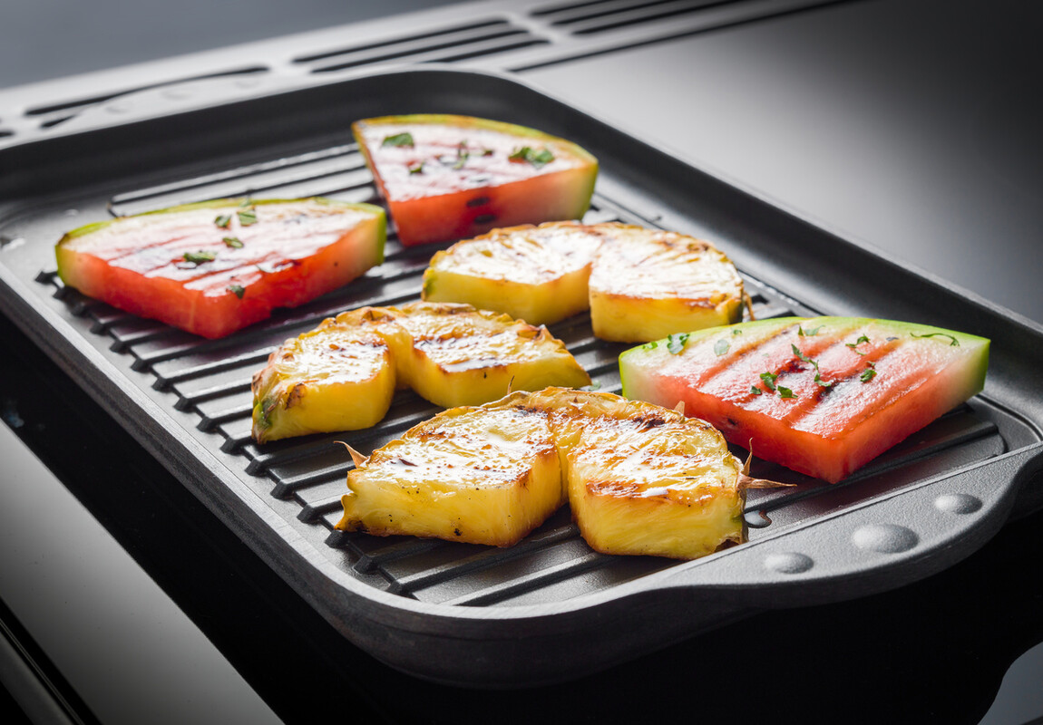 Gegrillte Ananas- und Wassermelonenstücke liegen nebeneinander auf einer Grillplatte und sorgen für eine leckere, fruchtige Beilage zum Grillen