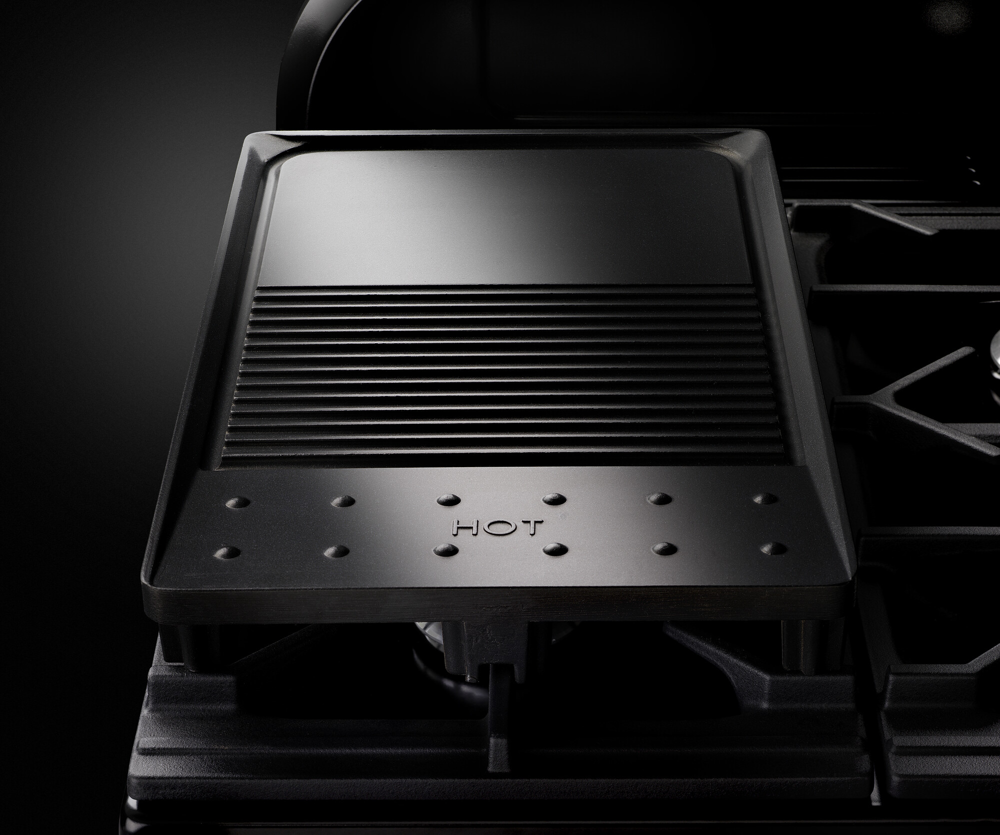 Schwarze gusseiserne Grillplatte auf einem Gasherd, ideal zum Grillen und Braten von Speisen, Vorderseite mit Markierung 'HOT'.