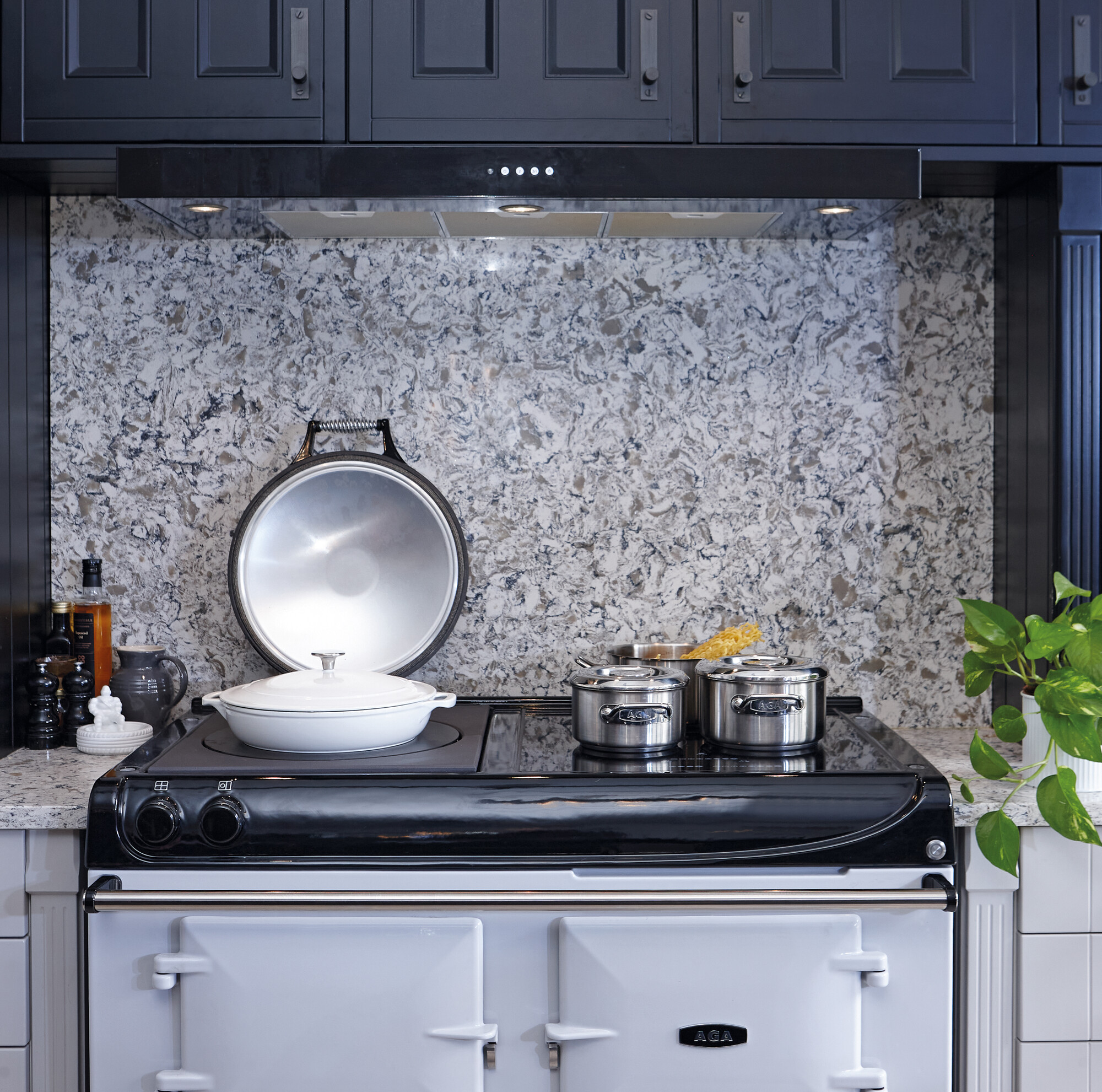 Moderner Herd mit weißen und Edelstahl-Kochtöpfen vor grauer Spritzschutzwand in stilvoller Küche