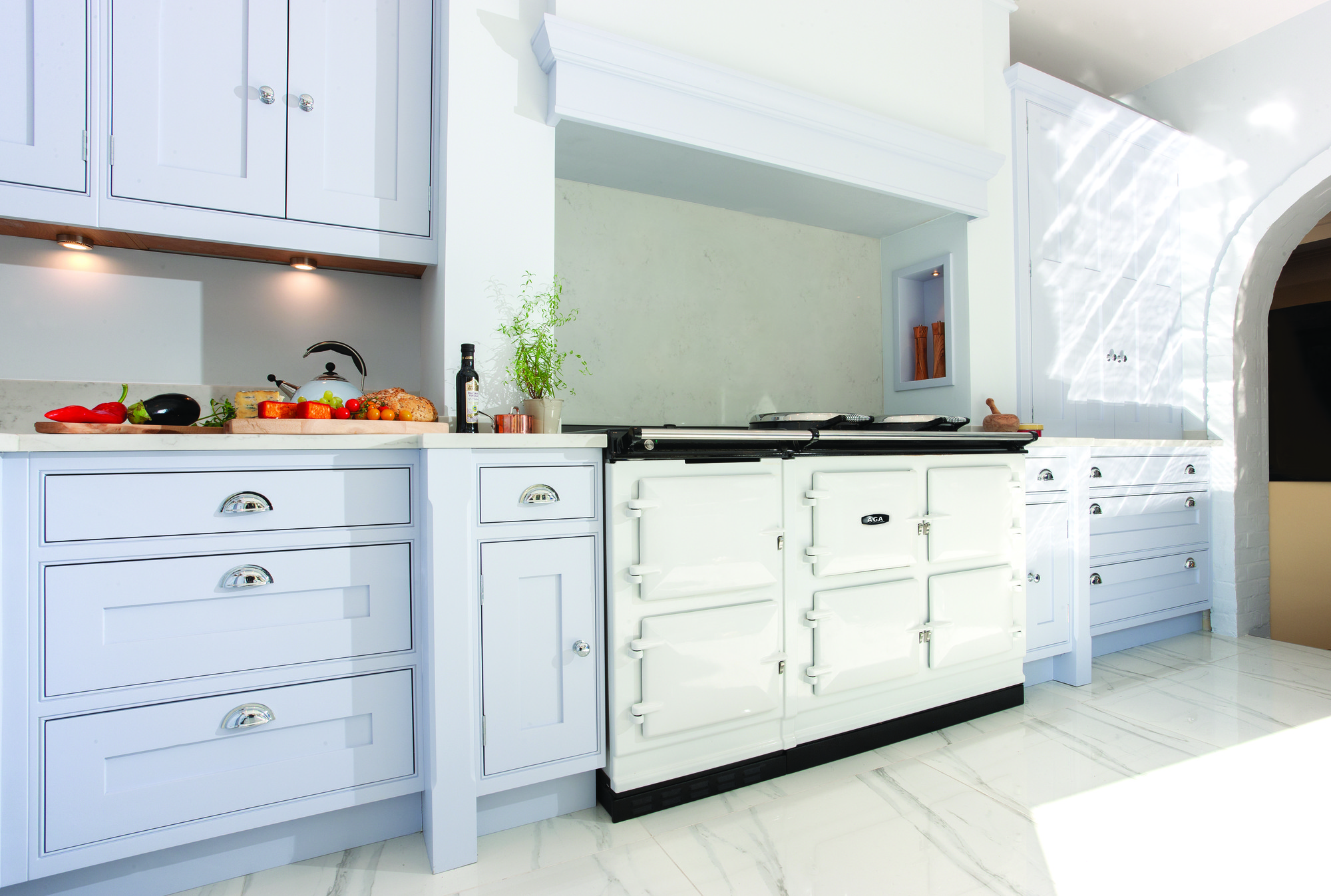 Helle Küche mit weißem AGA-Herd, hellblauen Schränken, Arbeitsfläche aus Marmor und Gemüse auf dem Schneidebrett