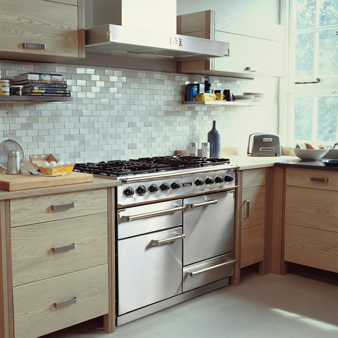 Küche mit Edelstahl-Gasherd, Dunstabzugshaube, hellen Holzschränken und Fliesenspiegel in Weiß
