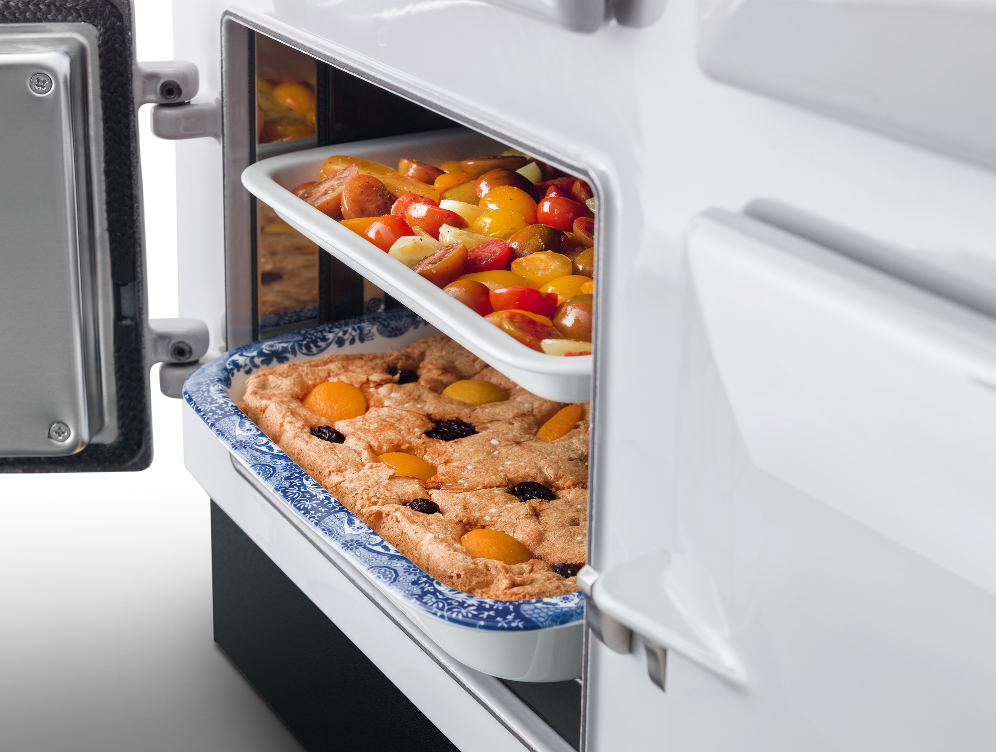 Zwei Auflaufformen im geöffneten Backofen, oben buntes Ofengemüse, unten ein Obstkuchen mit Aprikosen und Kirschen