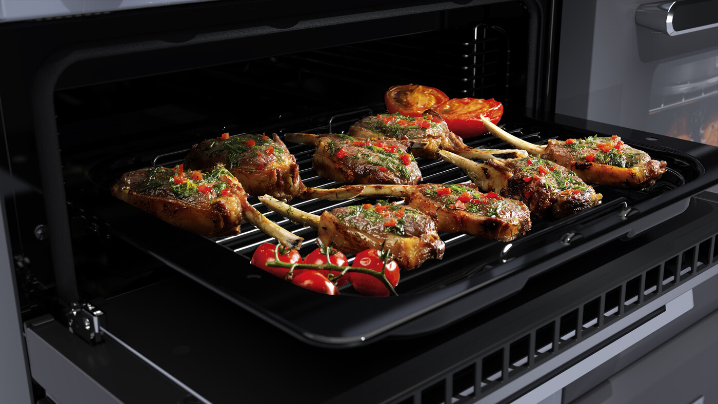 Nahaufnahme von saftigen Lammkoteletts mit frischen Kräutern und Paprika auf einem Grillrost im Backofen, daneben frische Tomaten