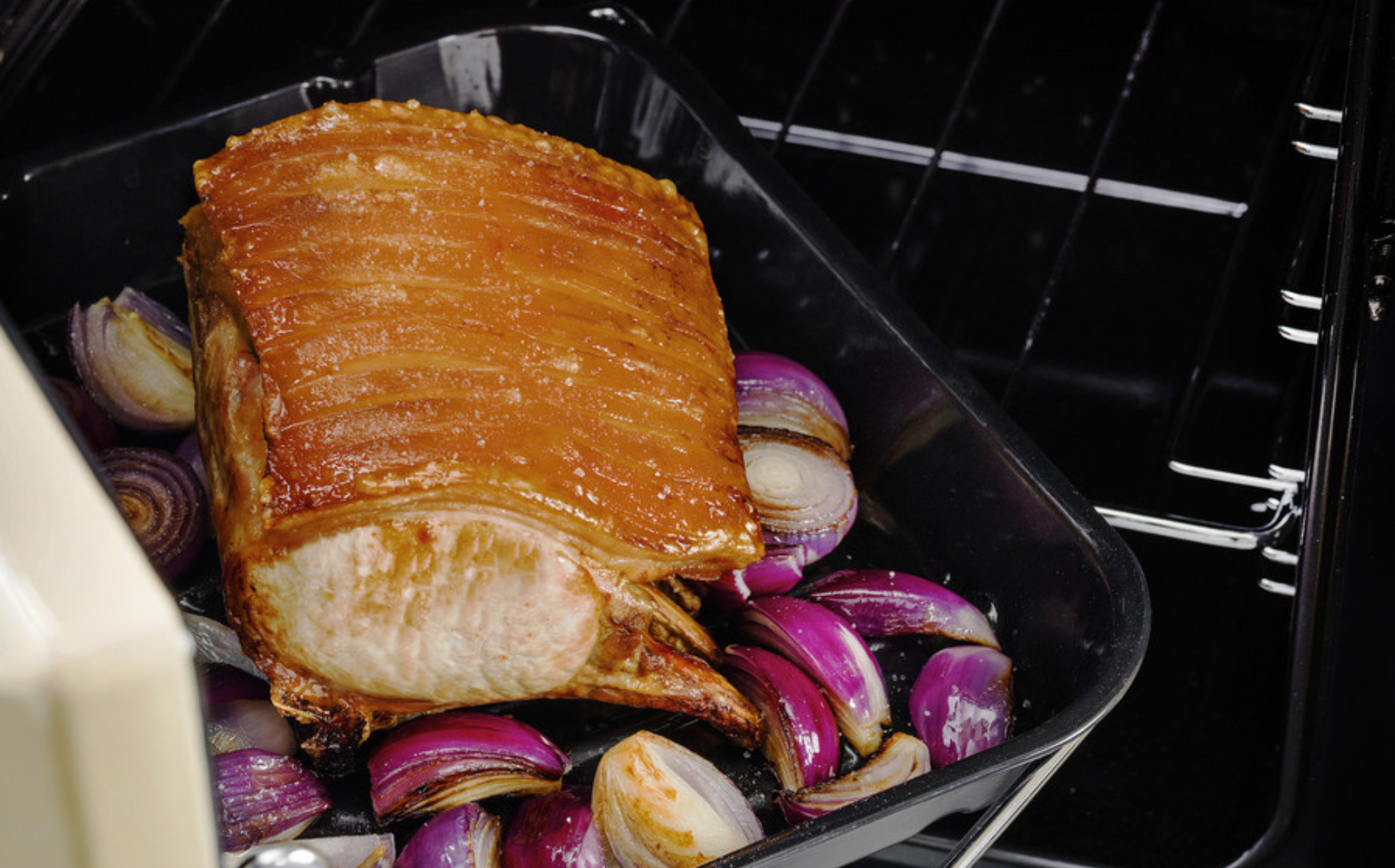 Schweinebraten mit krosser Kruste auf roten Zwiebeln in einer Bratform im Backofen