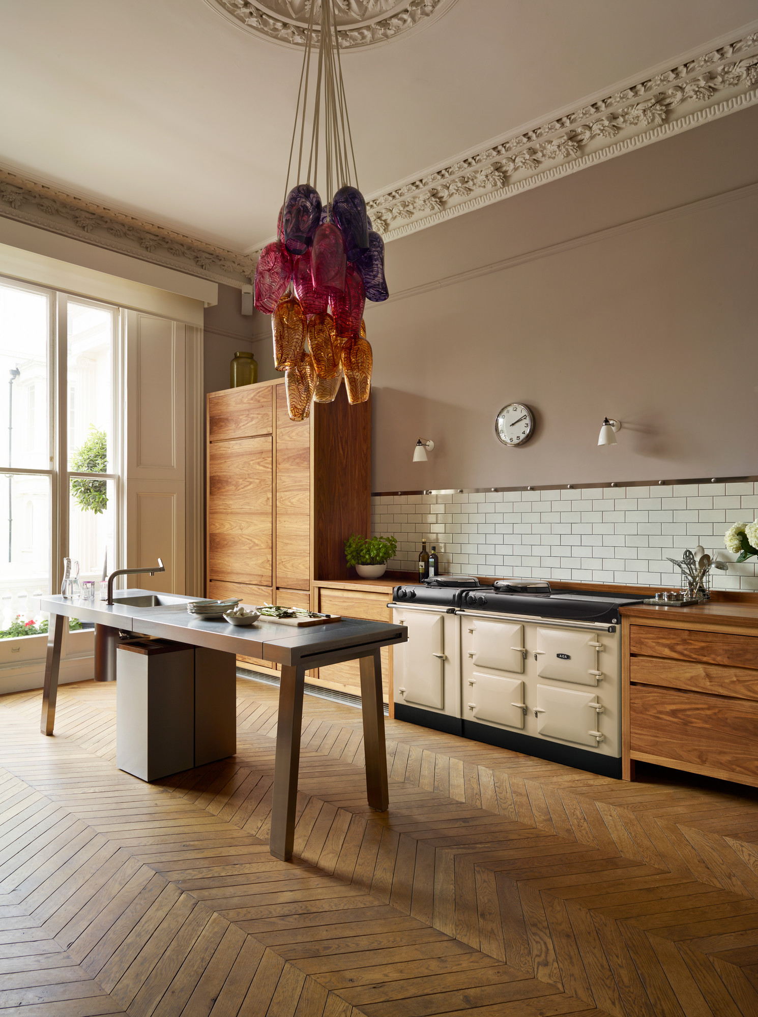 Helle, moderne Küche mit eleganten Holzmöbeln, großem Induktionsherd, Designer-Pendelleuchte aus buntem Glas und Parkettboden