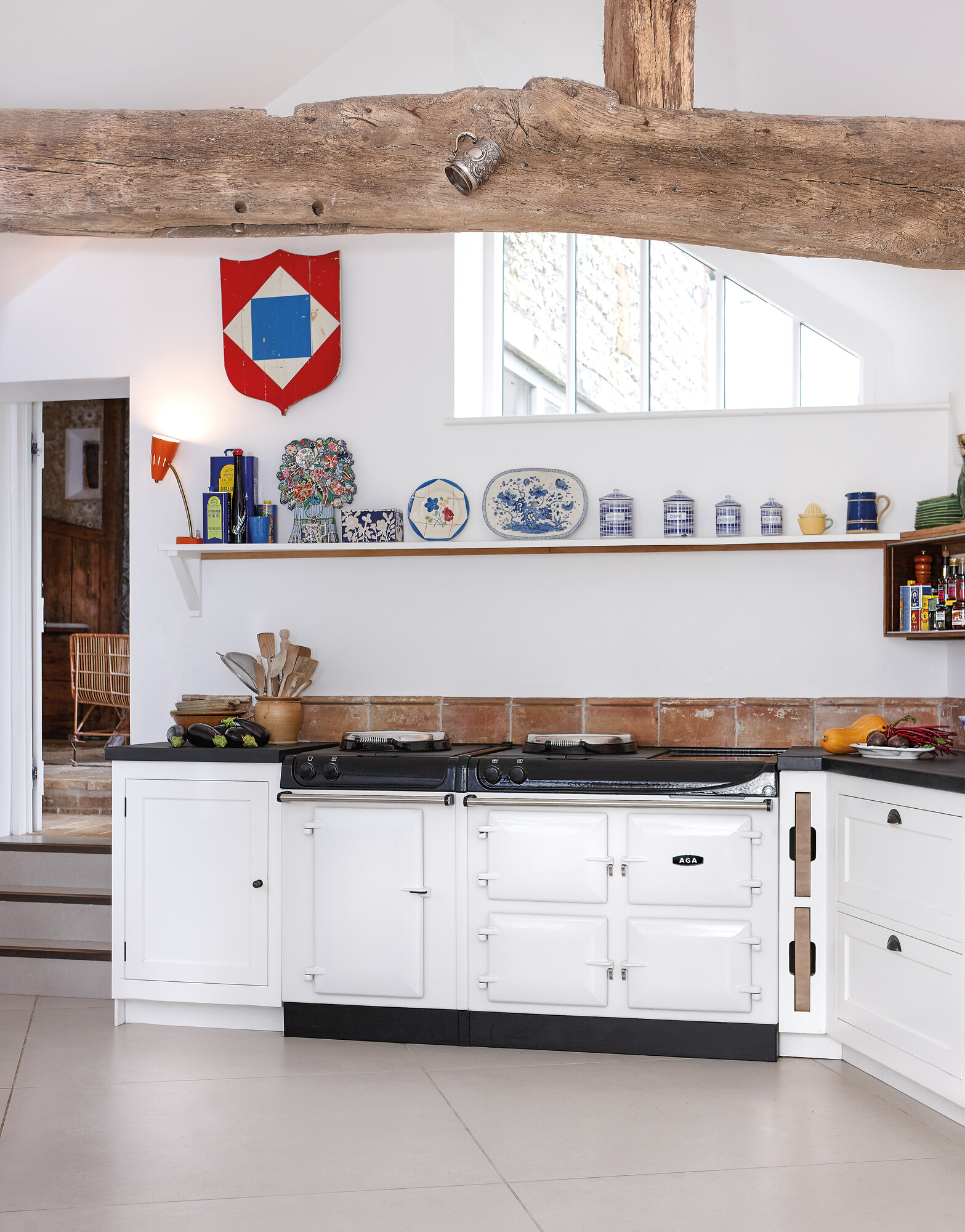 Helle, moderne Landhausküche mit weißem AGA-Herd, rustikalen Holzbalken und dekorativem Regal mit Teller- und Dosenarrangement