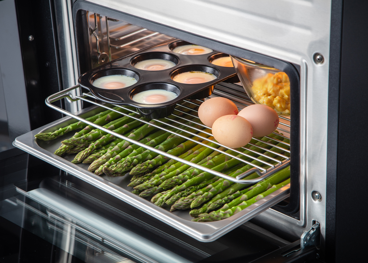 Grüner Spargel, ganze Eier und Muffinform mit gebackenen Eiern in einem Backofen auf Backblech und Gitterrost