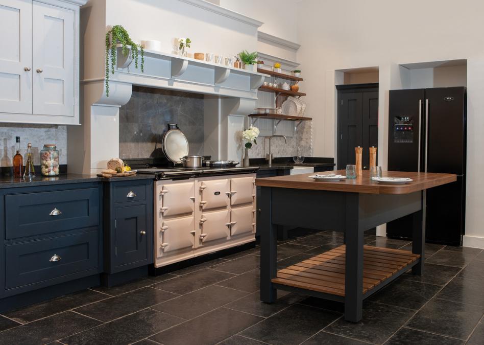 Große, stilvolle Landhausküche mit Kücheninsel, offenem Regal, cremefarbenem Herd und schwarzem Kühlschrank auf dunklem Fliesenboden