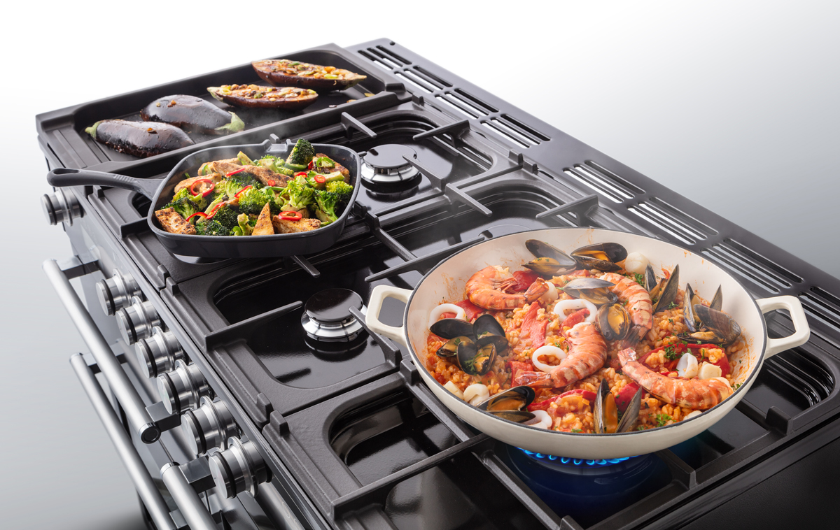 Gaskochfeld mit drei verschiedenen Gerichten: Pfanne mit Meeresfrüchte-Paella, Pfanne mit Brokkoli und Tofu sowie gratinierte Auberginen